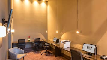 Una sala de conferencias con una larga mesa, varias sillas, un escritorio con computadora e impresora.