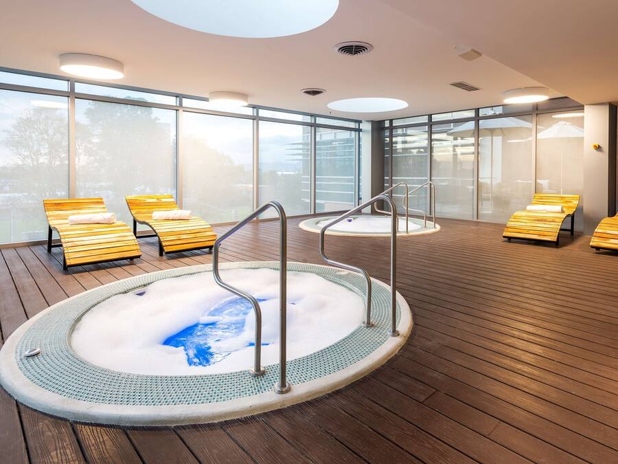 A modern indoor pool area with wooden loungers and a central hot tub.