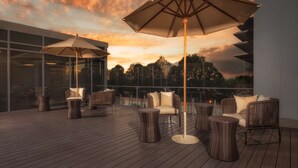Terraza en la azotea con mobiliario de mimbre, sombrillas grandes y barandilla de cristal con vistas al paisaje.