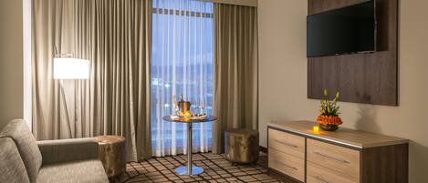 A hotel room with a sofa, a small round table with a candle, a cabinet, and a TV mounted on the wall.