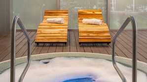 Un jacuzzi con dos sillones de madera, barandillas de metal y vistas a árboles a través de amplios ventanales.