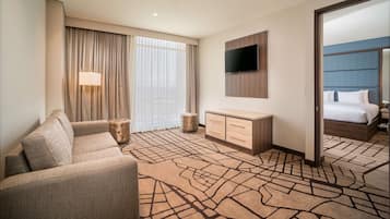 Une chambre d’hôtel avec un canapé, un téléviseur fixé au mur, un lit avec une tête de lit et un grand miroir.
