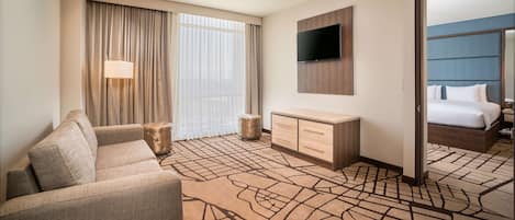 Habitación de hotel con sofá, televisor montado en la pared, cama con cabecera y un espejo grande.