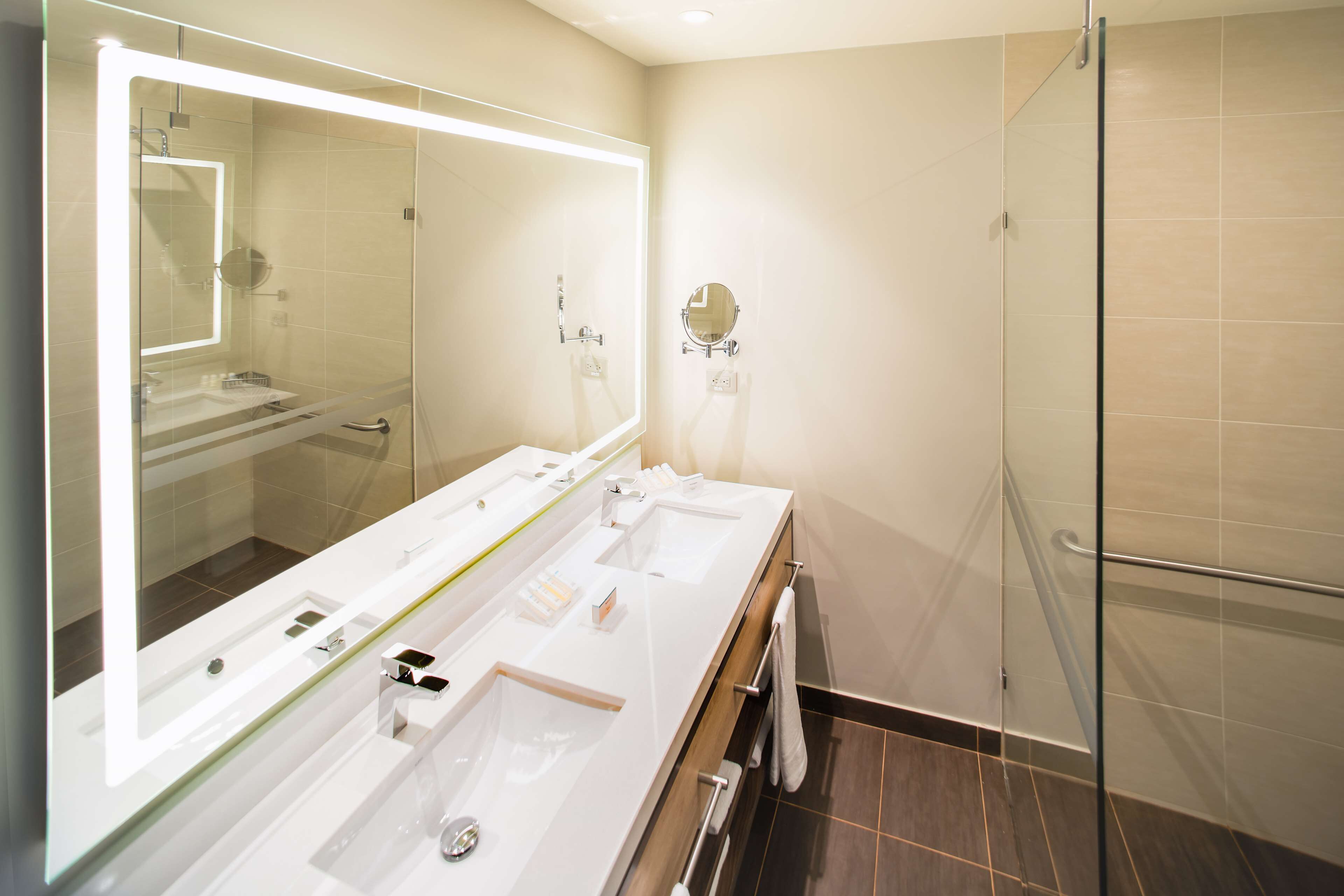 Un baño moderno con tres lavamanos, un espejo grande y una cabina de ducha de vidrio.