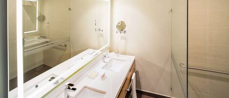 Un baño moderno con tres lavamanos, un espejo grande y una cabina de ducha de vidrio.