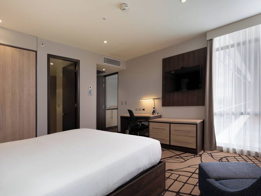 Een hotelkamer met een bed, bureau, stoel, televisie en grote ramen.