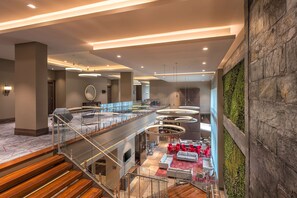A modern lobby with a glass staircase, a seating area with red chairs, and a green wall. - Hilton Garden Inn Bogota Airport (Bogotá)