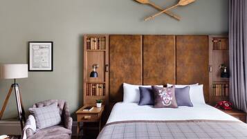 A hotel room with a large bed, a wooden headboard, a desk with a lamp, a chair, and a bookshelf.