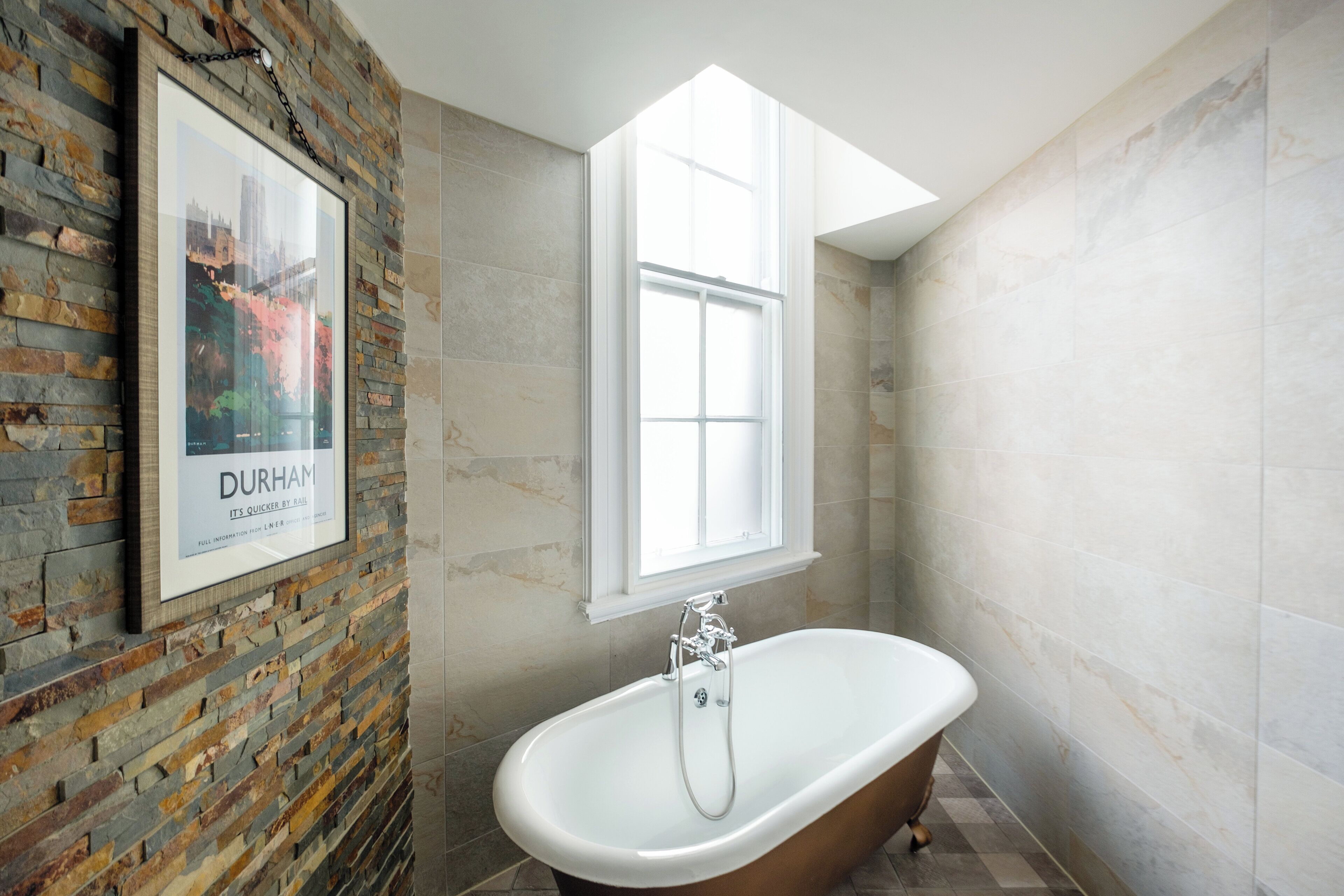A bathroom with a freestanding bathtub, a framed picture on the wall, and a window.