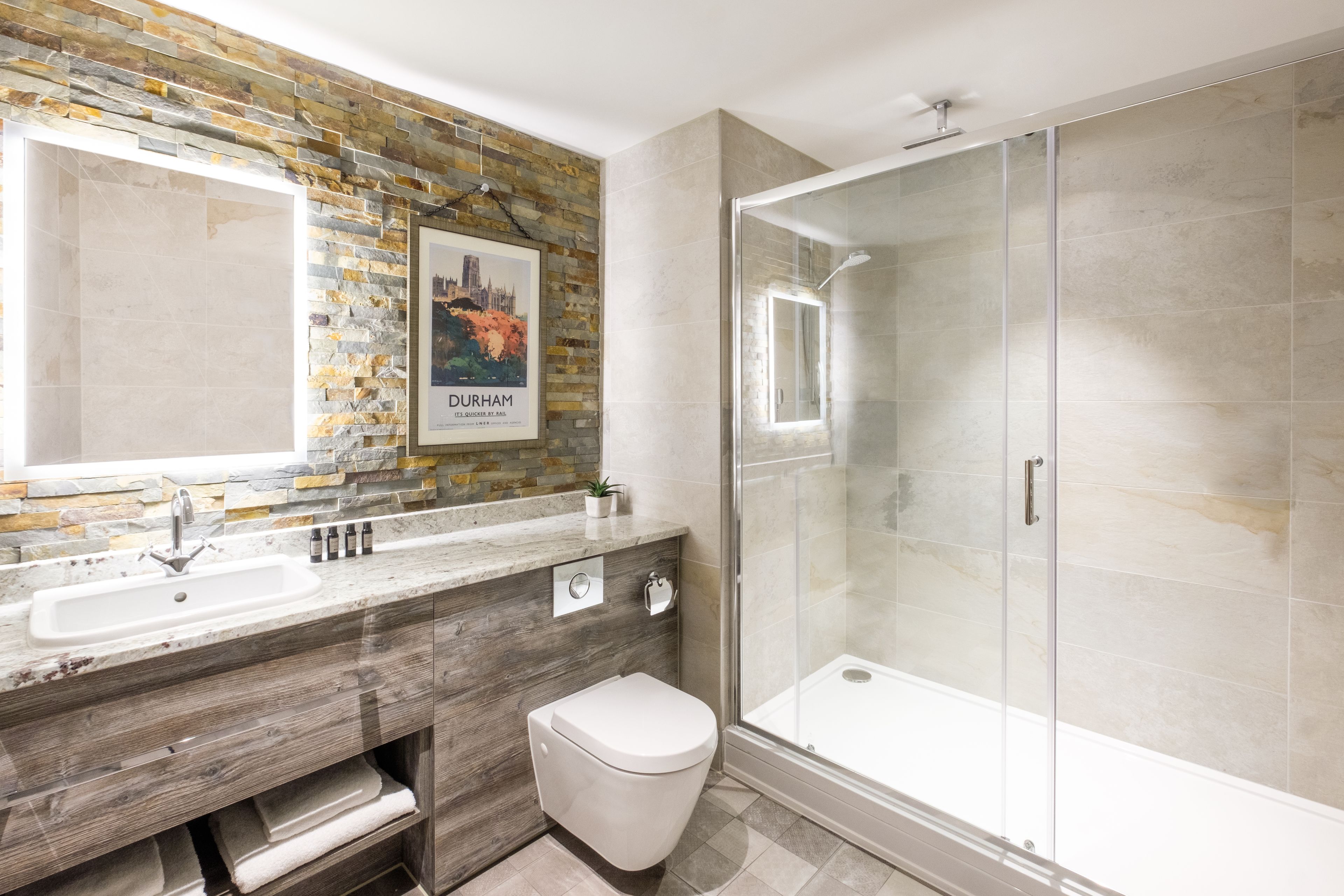 A modern bathroom with a stone mosaic backsplash, a large mirror, a sink, a toilet, and a glass-enclosed shower.
