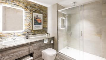A modern bathroom with a stone mosaic backsplash, a large mirror, a sink, a toilet, and a glass-enclosed shower.