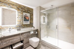 Une salle de bain moderne avec un mur recouvert d’une mosaïque de pierre, un grand miroir, un lavabo, des toilettes et une douche à parois de verre.