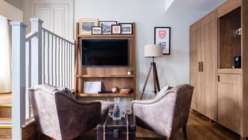 A living room with a wooden TV stand, two armchairs, a floor lamp, and a wooden cabinet.