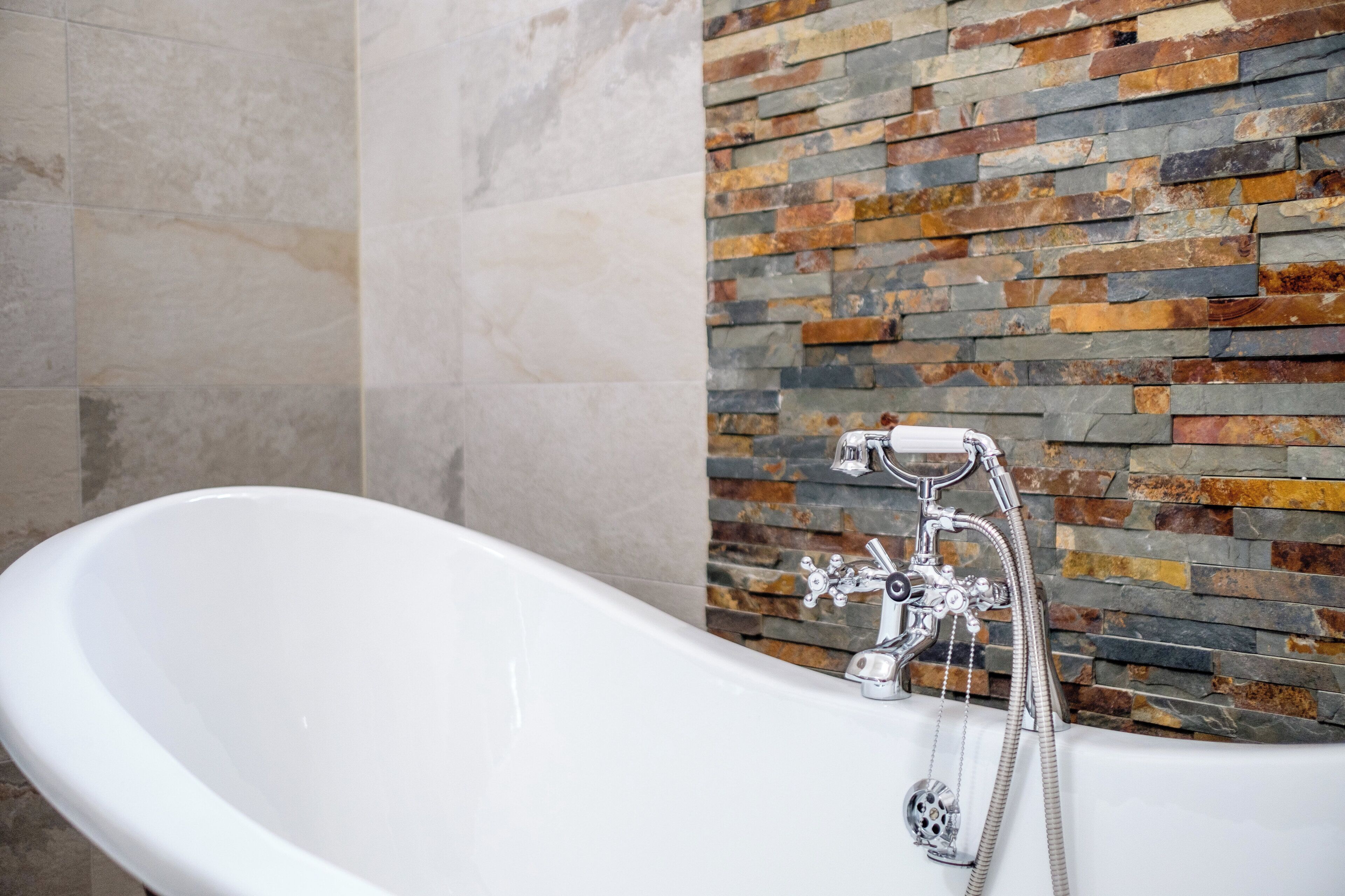 A modern bathroom with a freestanding bathtub, a stone mosaic wall, and a marble floor.