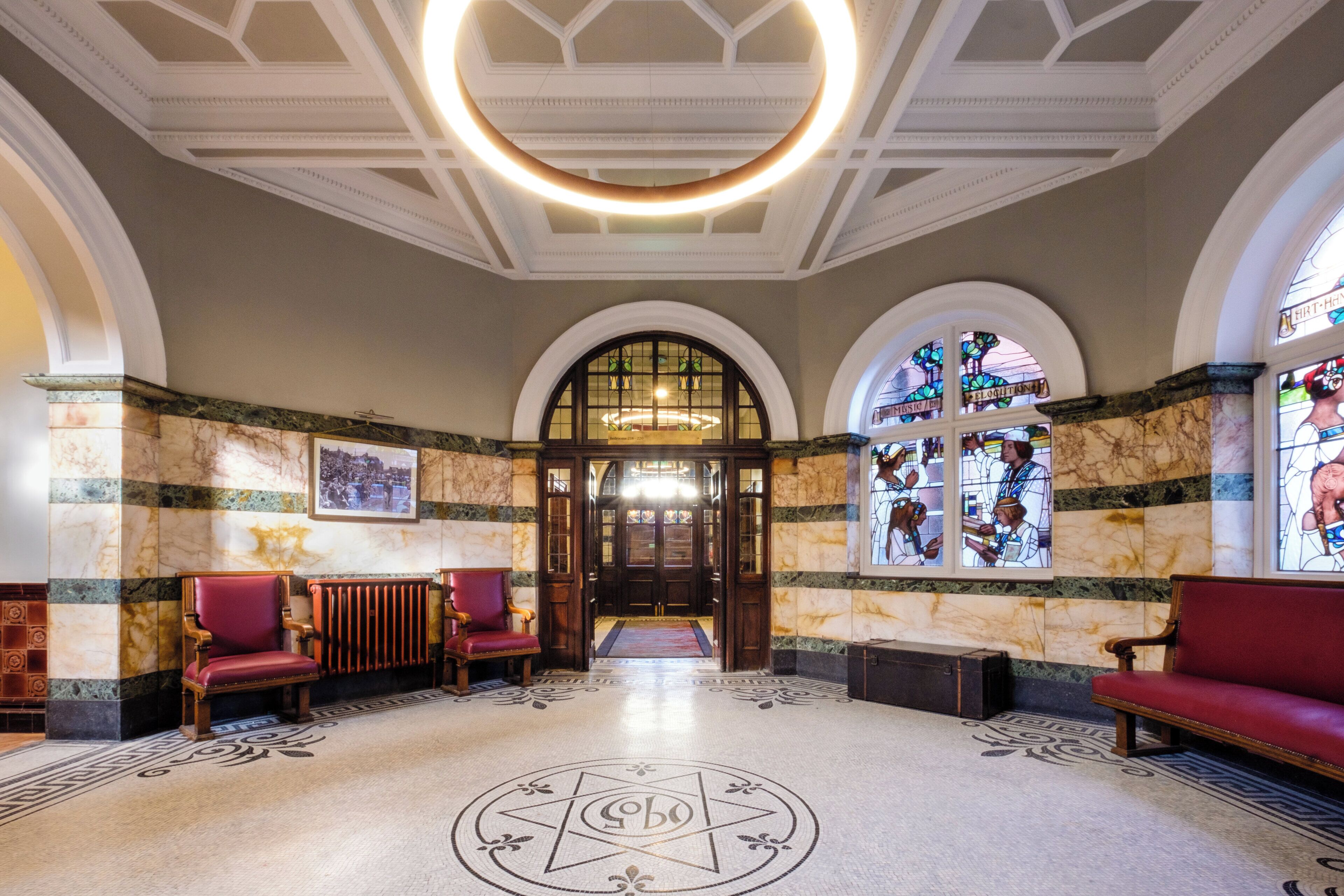 A grand lobby with a high ceiling, arched windows, and a central chandelier.