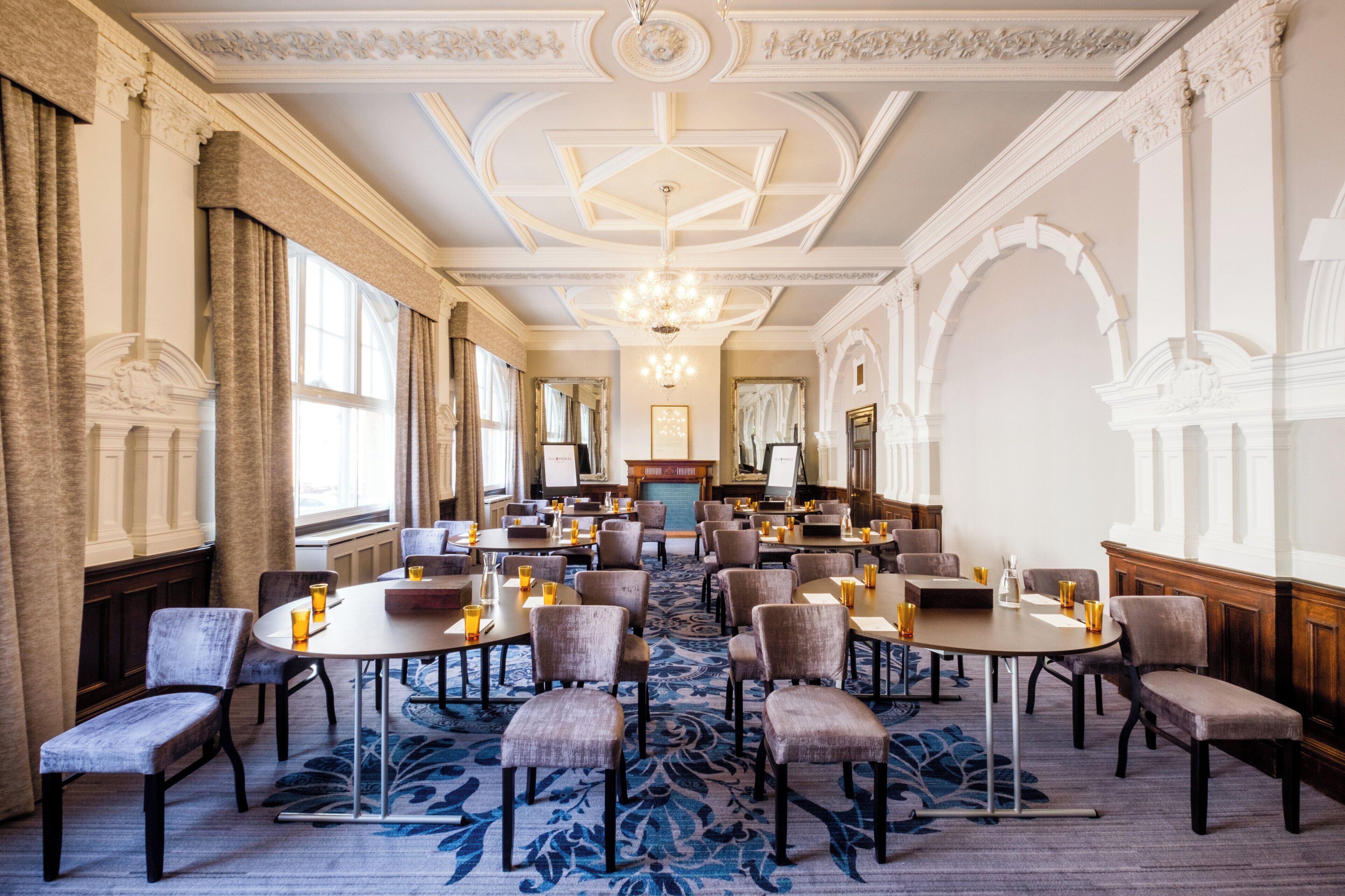 A hotel conference room with round tables, chairs, and a large chandelier.
