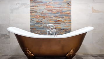 A freestanding bathtub with claw feet in a bathroom with a tiled floor and a mosaic wall.