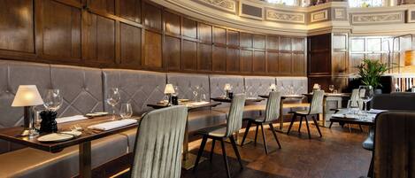 A formal dining area with wooden paneling, cushioned seating, and tables set for dining.