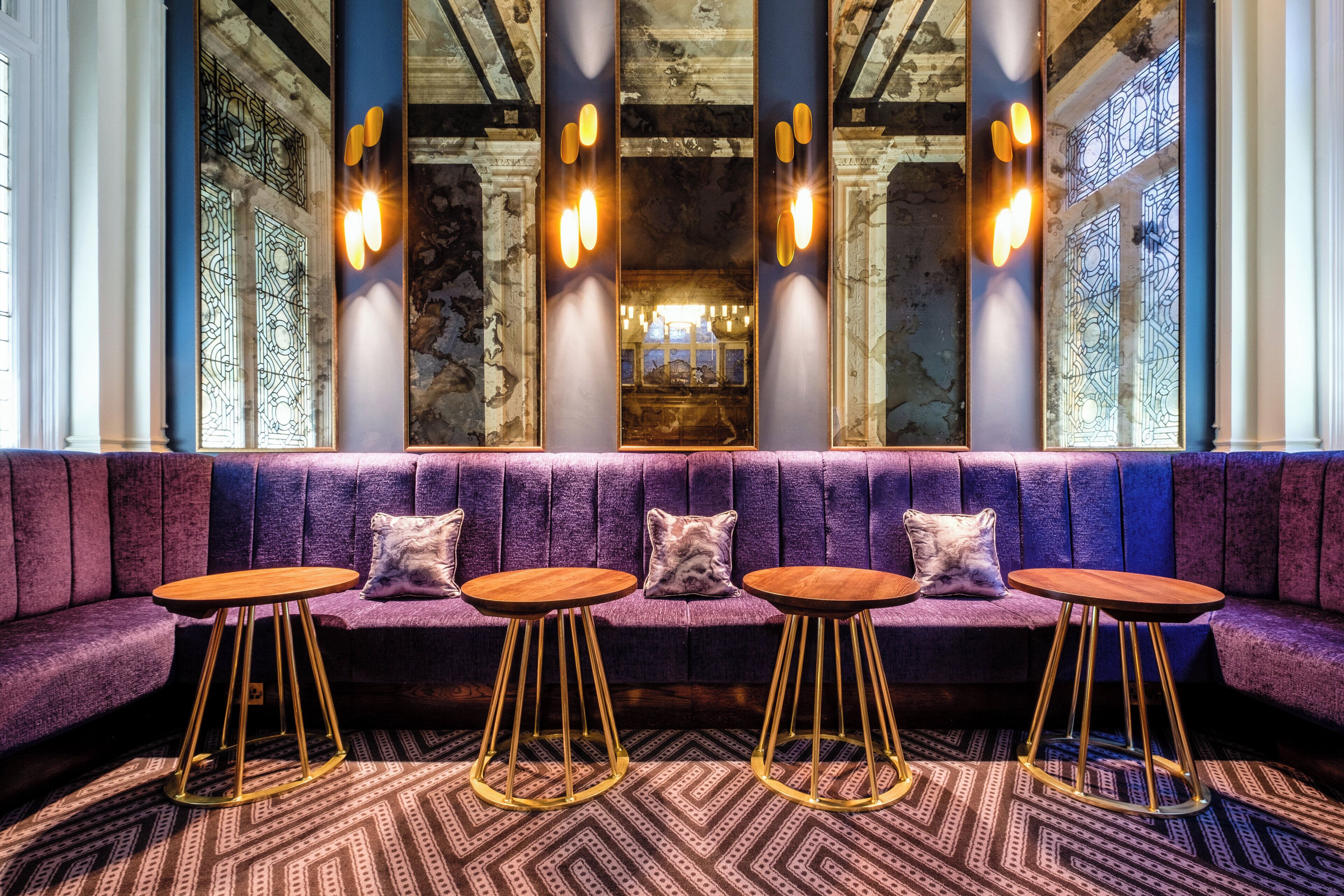 A seating area with a purple sofa and round tables with gold legs.
