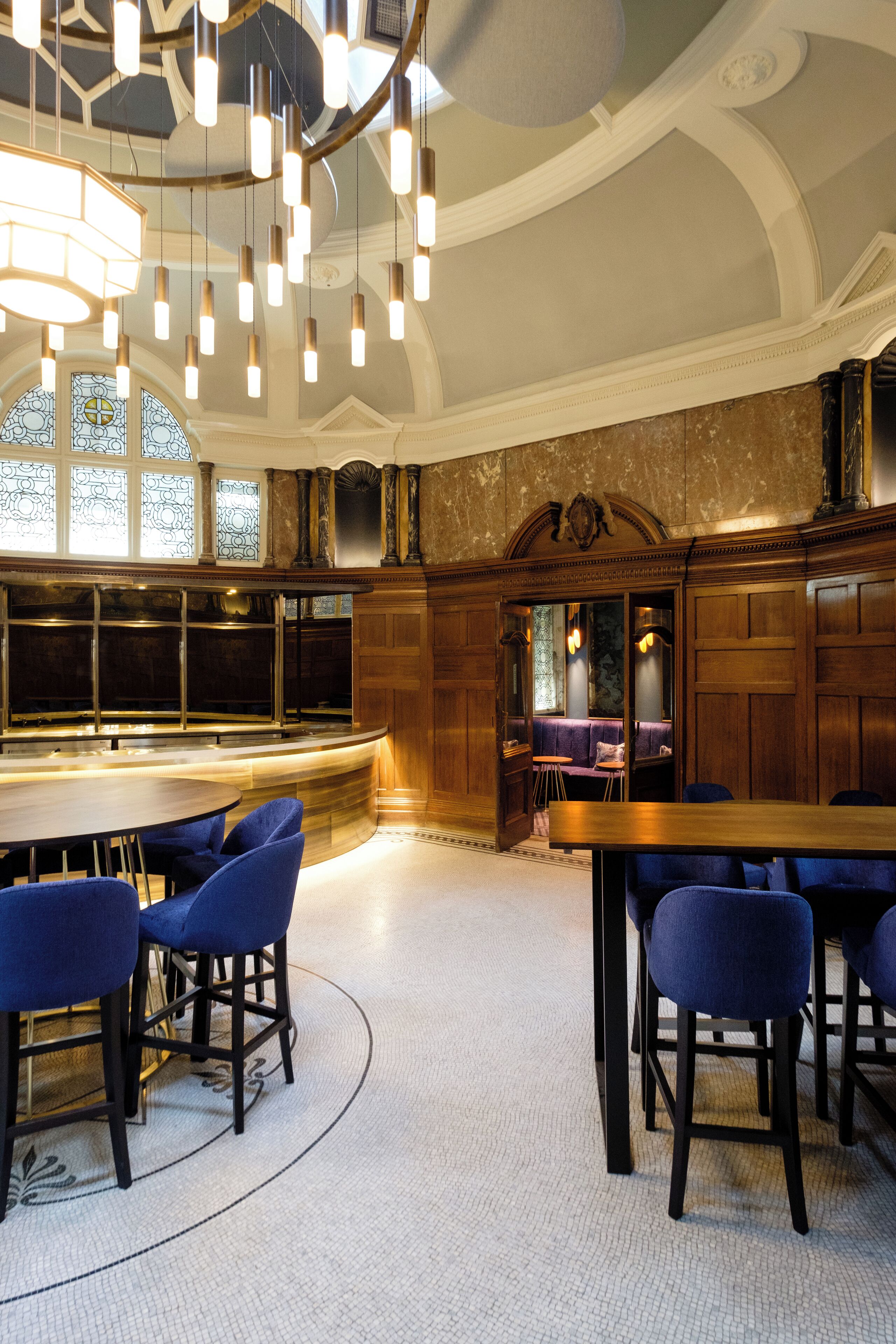 Un espace bar doté d’un comptoir incurvé, de tabourets de bar bleus et de luminaires suspendus.