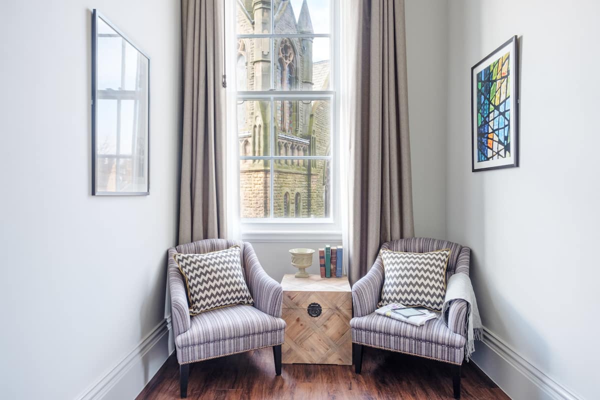 Une pièce comprenant deux fauteuils, une petite table en bois et une fenêtre avec des rideaux.