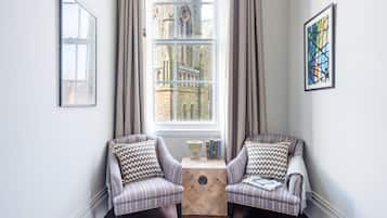 Una habitación con dos sillones, una mesita de madera y un ventanal con cortinas.