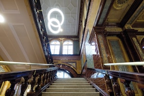 Una imponente escalera con barandales ornamentados y un candelabro circular en el techo.