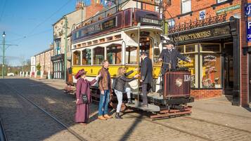 A vintage tram with passengers boarding, set against a backdrop of traditional brick buildings and a clear sky.