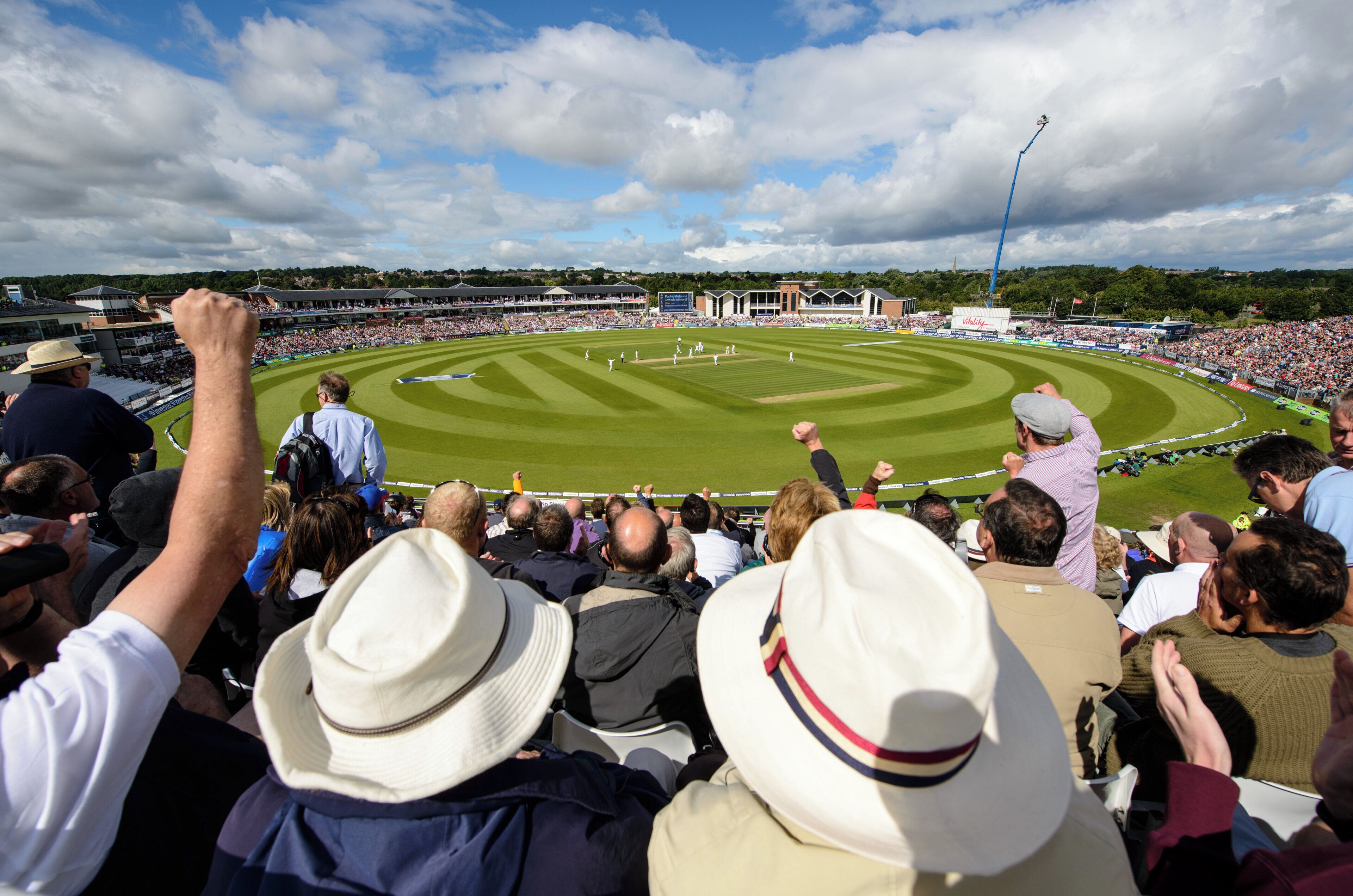 A stadium with a large crowd of spectators, a cricket pitch, and a floodlight tower.
