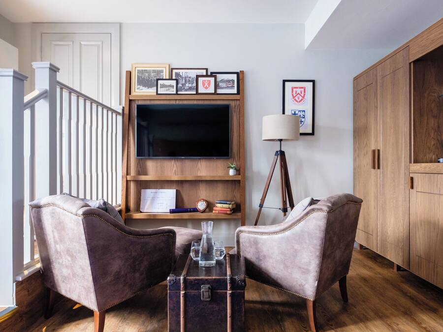 Een woonkamer met een trap, een televisie, een boekenkast, twee fauteuils, een salontafel en een kast.