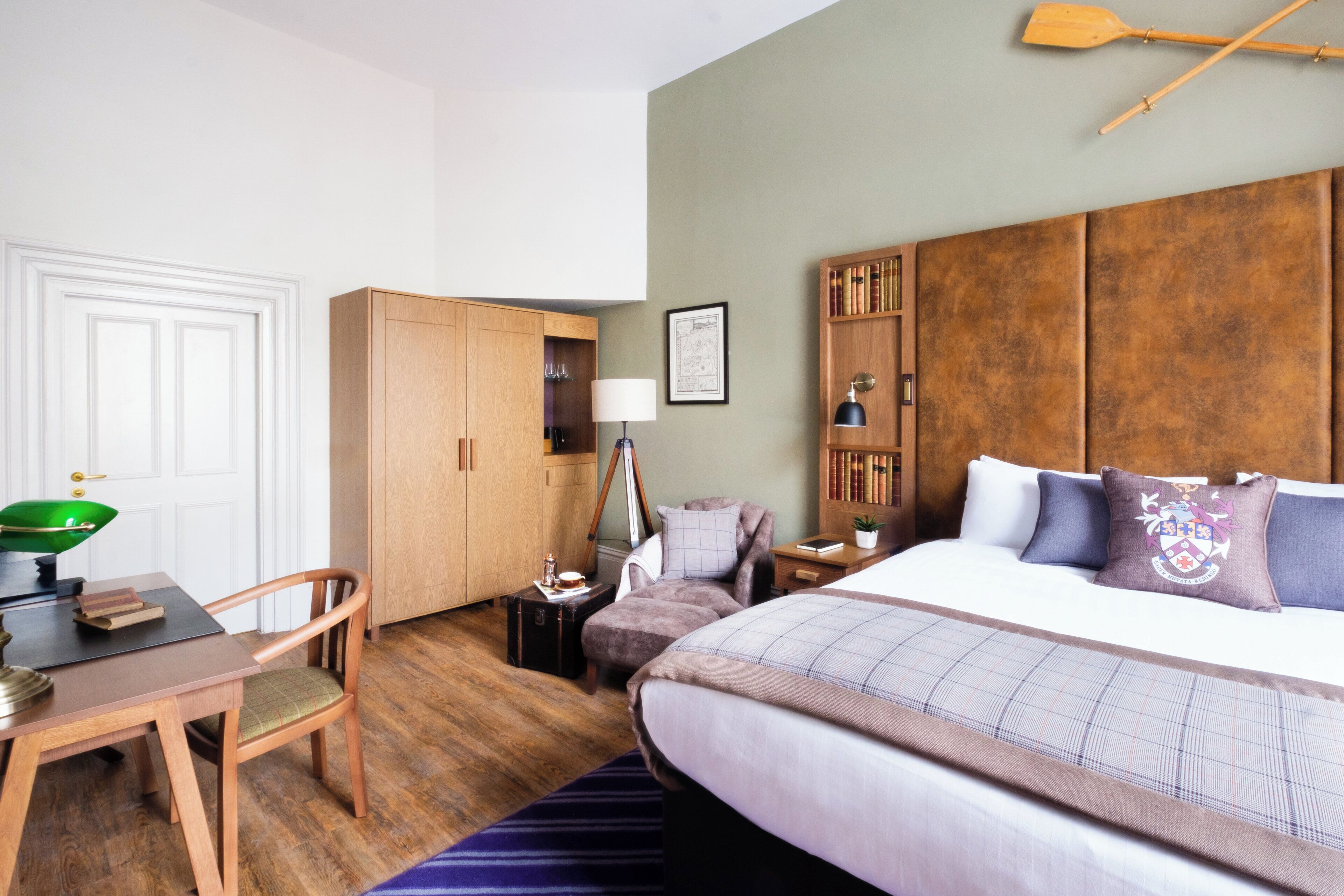 A hotel room with a bed, a desk, a chair, a wardrobe, and a bookshelf.