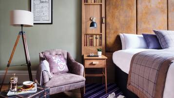 Une chambre d’hôtel avec un lit, une chaise, un bureau avec une lampe, une bibliothèque et une valise.
