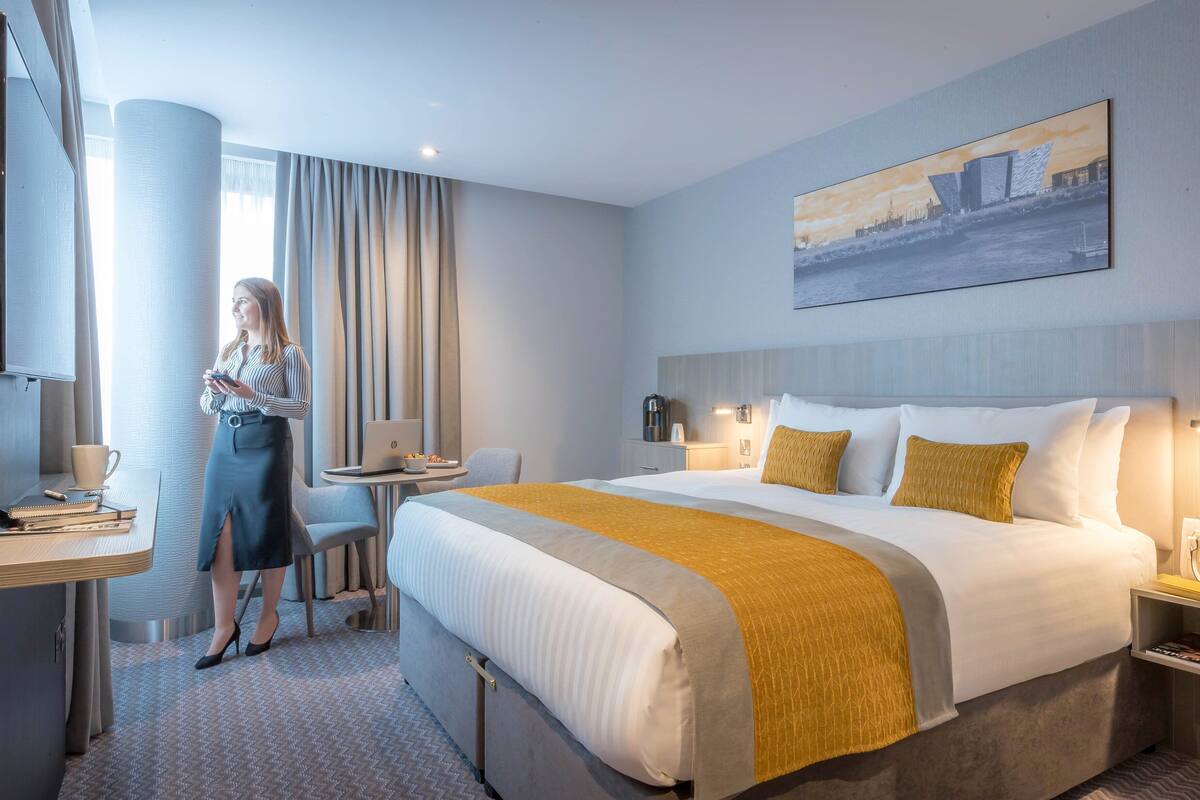 A hotel room with a large bed, a desk, a chair, and a window with curtains.