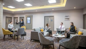 A conference room with a carpeted floor, modern furniture, and a digital screen on the wall.