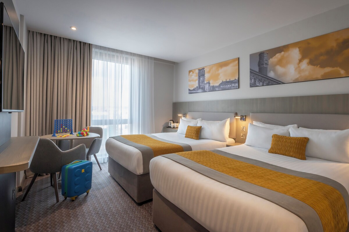 Een hotelkamer met twee bedden, een bureau, een stoel, een koffer en kunst aan de muren.