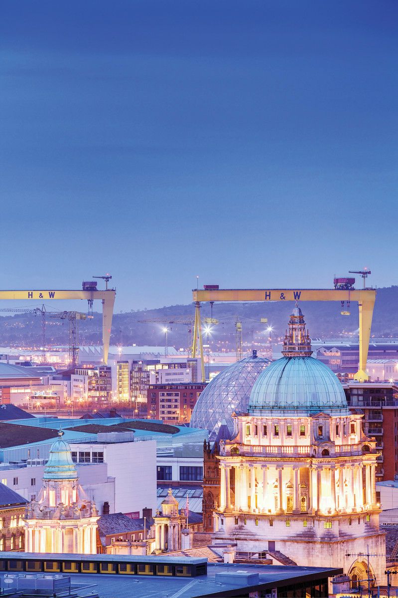A large, historic building with a prominent dome and classical architecture, situated in an urban setting with industrial elements in the background.