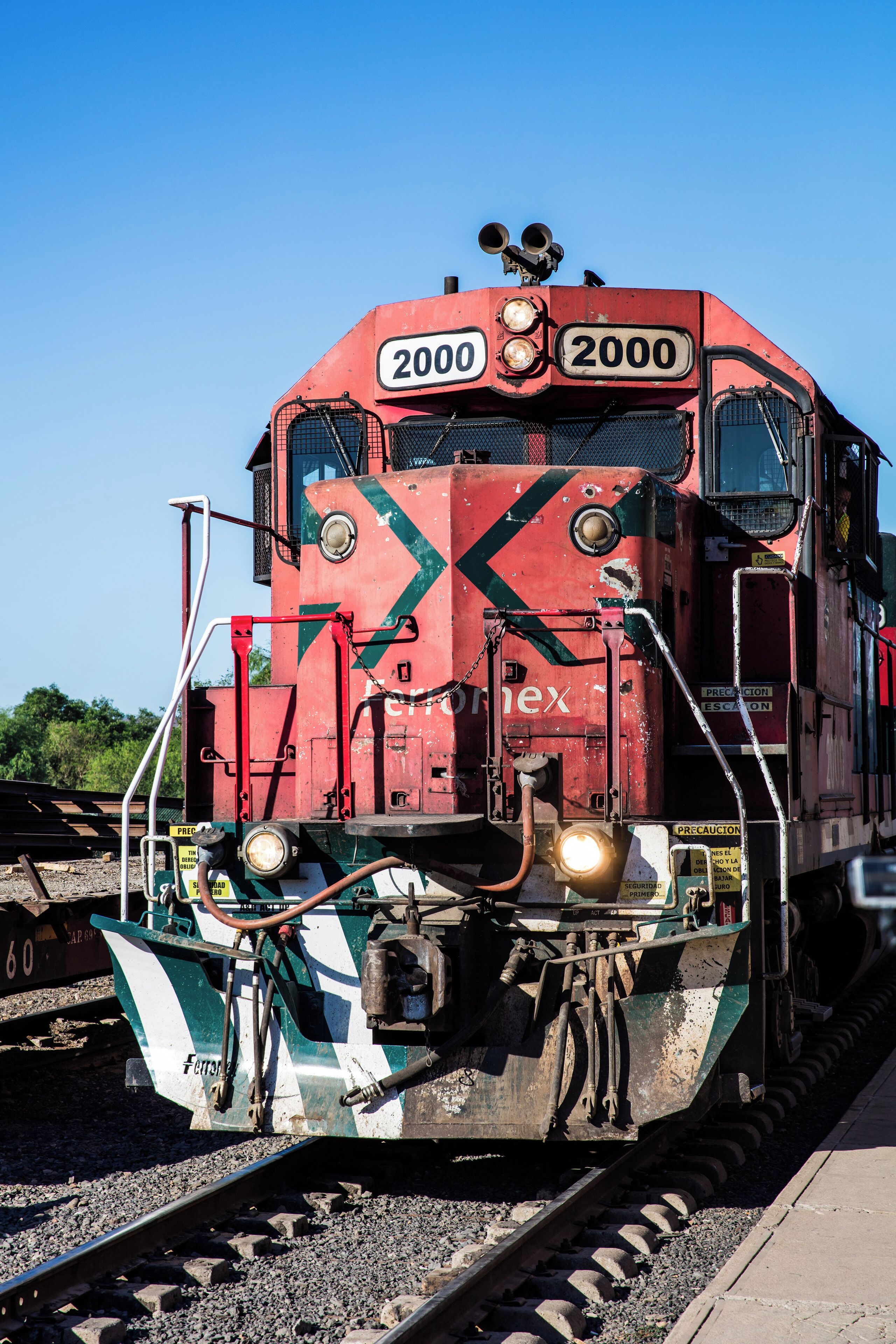Une locomotive rouge, portant le numéro 2000 sur sa façade, se déplace le long des voies ferrées.