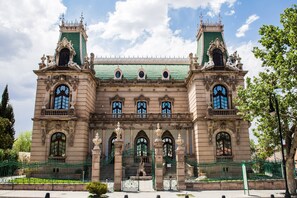 Un edificio histórico con arquitectura ornamentada, amplias ventanas de arco y techo verde.