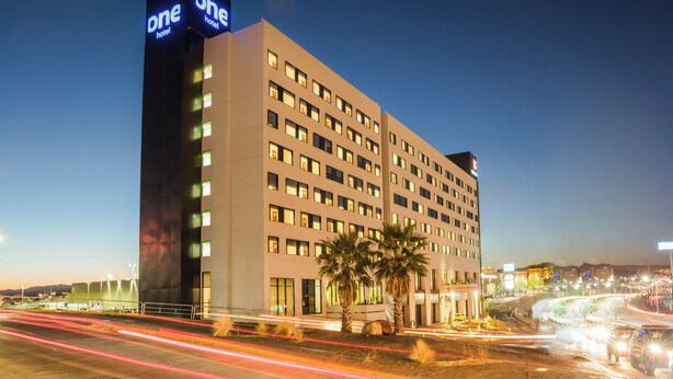 Un hotel de varios pisos con un llamativo letrero 'One Hotel', que presenta un diseño arquitectónico moderno con fachada plana y numerosas ventanas.
