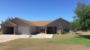 A two-story brick house with a garage, a front yard with a small tree, and a clear blue sky. - Amistad Lake House Del Rio Tx (Del Rio)