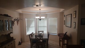 A dining area with a table and chairs, a chandelier, and windows with blinds. - Amistad Lake House Del Rio Tx (Del Rio)