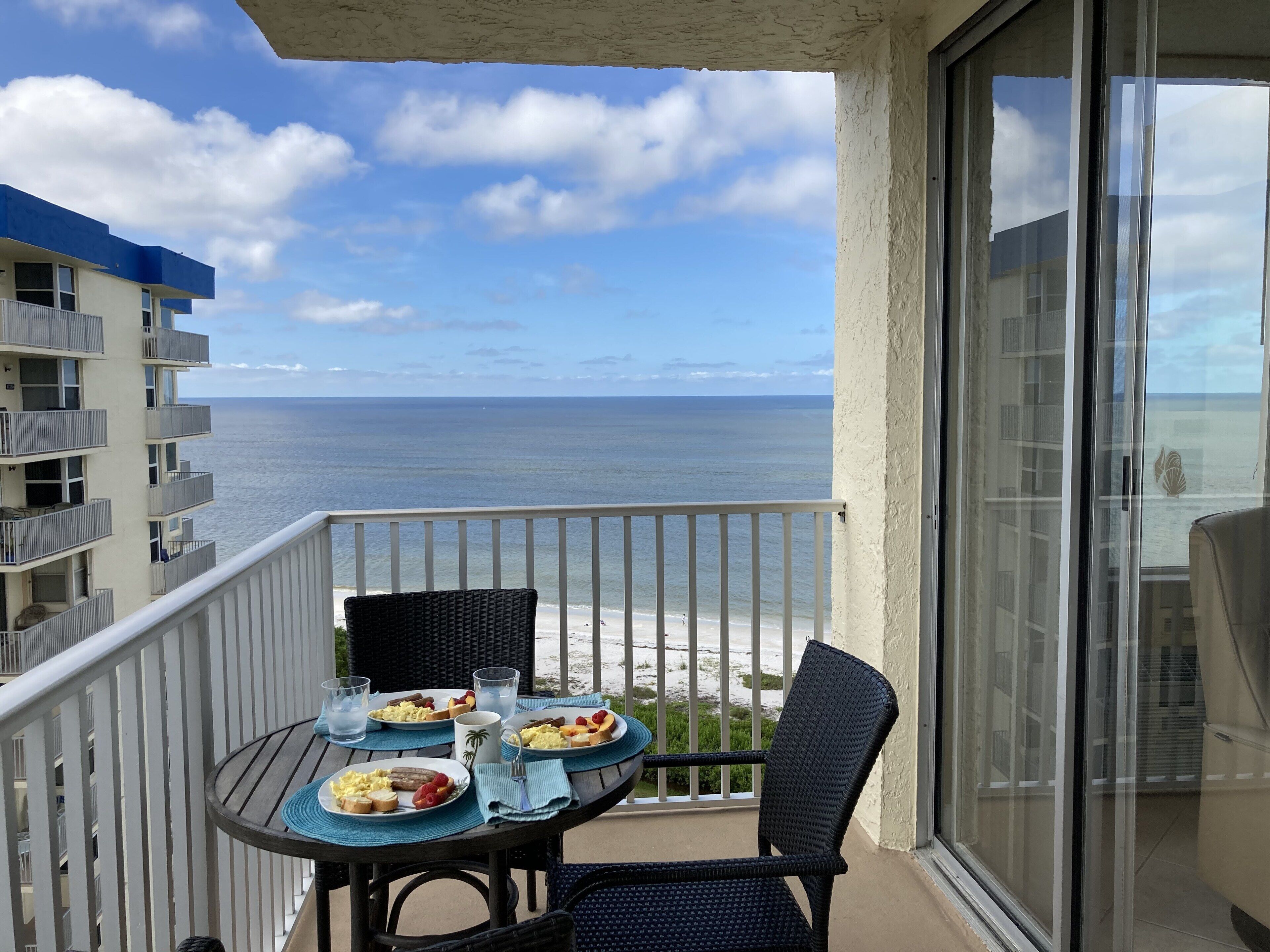 A balcony with a table set for breakfast overlooking the ocean.