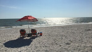 Een strand met een rode parasol, twee strandstoelen en een koelbox.