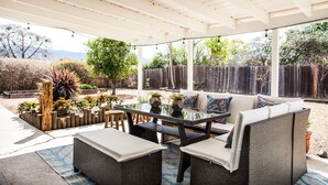 Un patio couvert aménagé avec des meubles en osier, une table en verre et des plantes en pot.