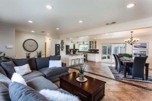 A spacious living room with a sectional sofa, a coffee table, and a dining area with a table and chairs. - Modern Newbury Park Home| Netflix| Quiet| Safe| Meticulously Clean (Newbury Park)