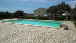 A swimming pool with a stone-tiled deck, surrounded by greenery and a building with a flat roof. - 5F Studio with swimming pool (Modica)