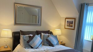 A bedroom with a bed, two bedside tables, a mirror, a picture on the wall, and a window with curtains. - The Grange, Portrush. Deluxe holiday home, 8 beds, up to 12 guests, 6 bedrooms.  (Portrush)