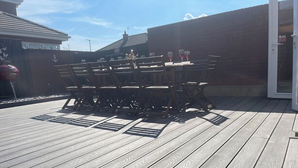 A wooden deck with a table and chairs, a brick wall, and a door. - The Grange, Portrush. Deluxe holiday home, 8 beds, up to 12 guests, 6 bedrooms.  (Portrush)