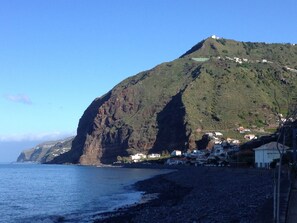 A coastal landscape with a prominent cliff, a beach, and a settlement with white buildings.