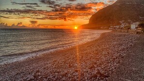 A beach with a sunset, rocky shore, and a mountain in the background. - Apartment "Vai Vem" -T2 on the island of Madeira - Portugal Tourism 32408 / AL (Madalena do Mar - Madeira)